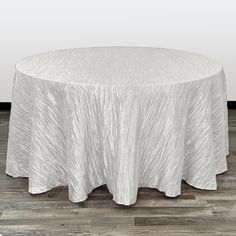 a round white table with a silver cloth on it's top and wood flooring