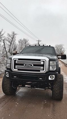 a large truck driving down a dirt road next to power lines and telephone poles on a cloudy day