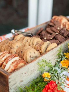 an assortment of cookies and pastries in a wooden box on a table with flowers