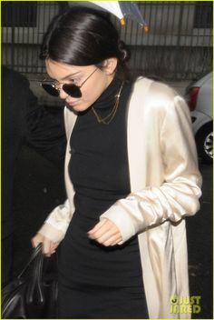 a woman in a black dress and white blazer carrying a handbag while walking