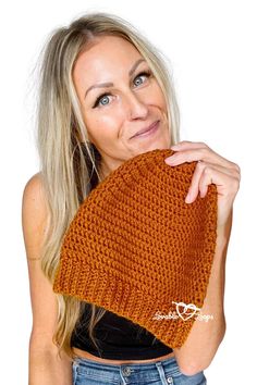 a woman wearing a brown knitted beanie with her hand on her face and looking at the camera