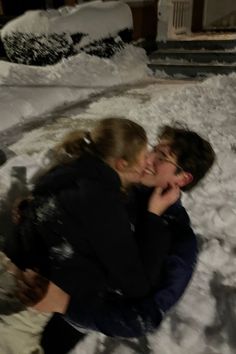 two people sitting in the snow hugging and kissing each other with their faces close together