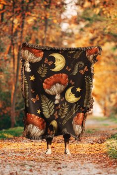 a black blanket with mushrooms and stars on it in the middle of a road surrounded by trees