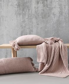 two pillows and a blanket on a wooden bench in front of a concrete wall,