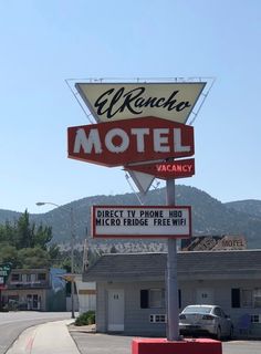 a motel sign on the corner of a street with mountains in the background and cars parked nearby