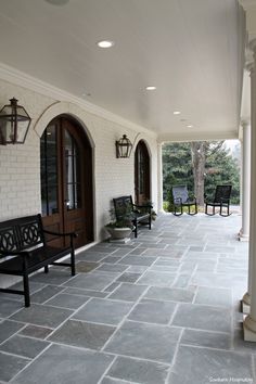 an empty porch with chairs and lights on the outside wall, along with stone flooring