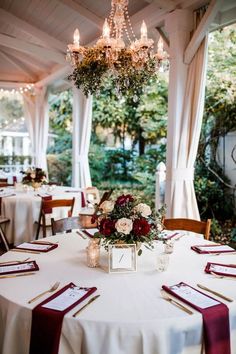 a dining room with tables and chairs covered in white tablecloths, chandeliers and flowers