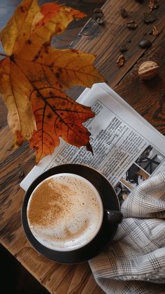 a cup of coffee sitting on top of a wooden table next to an open newspaper