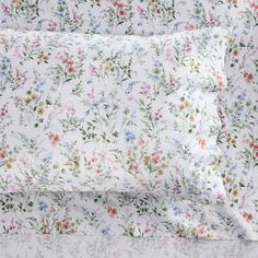 a white sheet with flowers on it is laying next to a pillow case and blanket