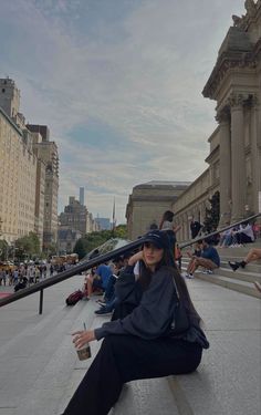 a woman sitting on the ground in front of a building with people walking around her