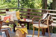 an outdoor deck with chairs, tables and fire pit in the middle surrounded by trees