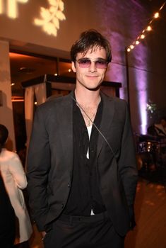 a man in a suit and sunglasses standing next to a wall with lights on it