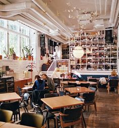 people sitting at tables in a restaurant with lots of bottles hanging from the ceiling above them