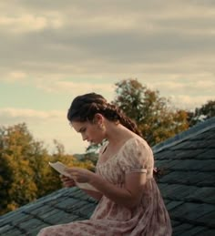 a woman sitting on top of a roof looking at a piece of paper in her hand