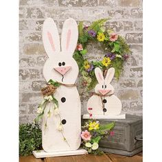 two wooden rabbits are standing next to each other in front of a wreath with flowers