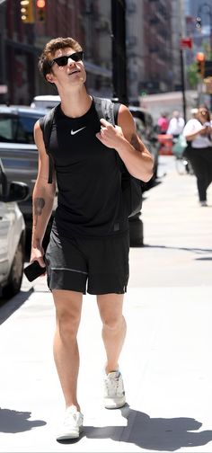 a man in black shirt and shorts walking down street with his hand on his hip