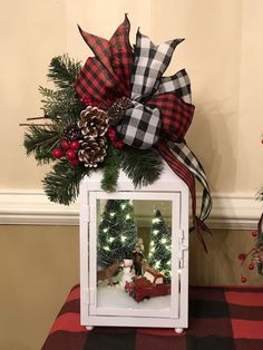 a small christmas scene is displayed in a white box with red and black plaid ribbon