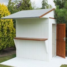 a small white shed with a wooden door and window on the side, in front of some bushes