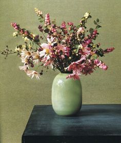 a green vase filled with lots of pink and white flowers on top of a table