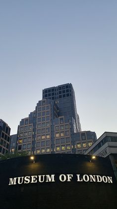 the museum of london sign is lit up in front of tall buildings at dusk time