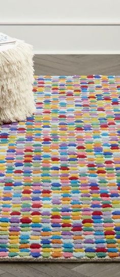 a multicolored rug on the floor with a white poufce sitting next to it