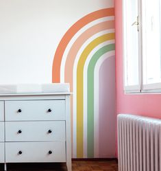 a baby crib next to a wall with a rainbow painted on it's side