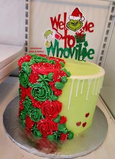 a green and red decorated cake sitting on top of a metal platter next to a sign