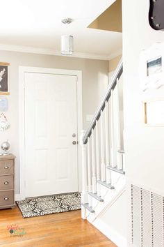 a white door and some stairs in a room with wood floors, rugs and pictures on the wall