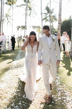 a man and woman walking down a path in front of palm trees with confetti on the ground