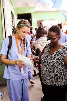 two women in scrubs are looking at something on a piece of paper while others stand around