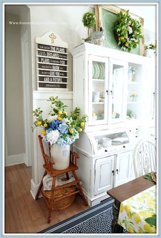 a white china cabinet with flowers on it in the corner of a dining room area