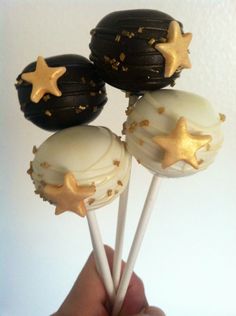 hand holding three chocolate cake pops with gold star decorations on them and white frosting