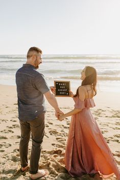 a man and woman standing on top of a beach next to the ocean holding an award plaque