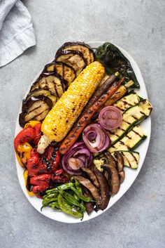 grilled vegetables and corn on the cob are arranged on a white platter