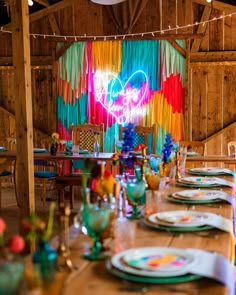 a table set up for a party with plates and utensils in front of a heart - shaped neon sign