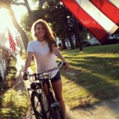 a woman riding a bike down a street next to a red and white striped flag