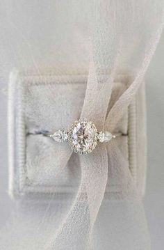 an engagement ring sitting on top of a white piece of cloth with a bow around it