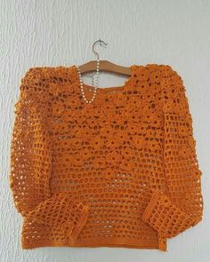 an orange crocheted sweater hanging on a white wall