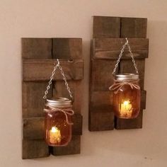 two mason jars are hanging on the wall with chains attached to them and one is filled with candles