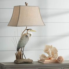 a bird lamp sitting on top of a table next to a book and sea shells