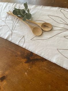 two wooden spoons sitting on top of a white table cloth with leaves and branches