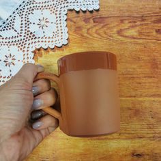 a hand holding a coffee cup on top of a wooden table next to a doily