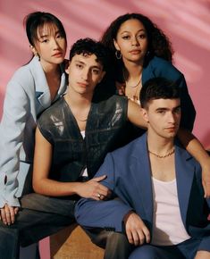 three people sitting next to each other in front of a pink wall and one person wearing a blue jacket