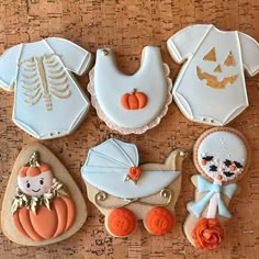 decorated cookies are arranged in the shape of baby's clothes and pumpkins on a table