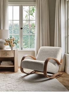 a living room with a rocking chair, table and large window in it's corner