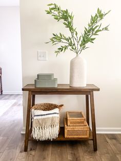 a wooden table topped with a white vase filled with green leaves next to two wicker baskets