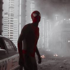 a man in a red spider suit standing next to a police car