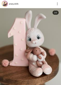 a pink number one cake topper with a bunny holding a teddy bear in front of it