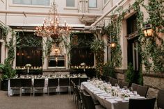 an indoor dining area with tables, chairs and chandeliers covered in greenery