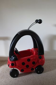 a red and black toy car sitting on top of a carpeted floor next to a white wall